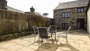 A stone building with a tiled patio, outdoor seating, and a stone wall. - The Byre (Grange-over-Sands)