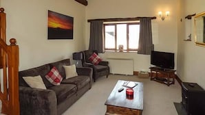 A cozy living room with a fireplace, a television, and a painting on the wall. - The Byre (Grange-over-Sands)