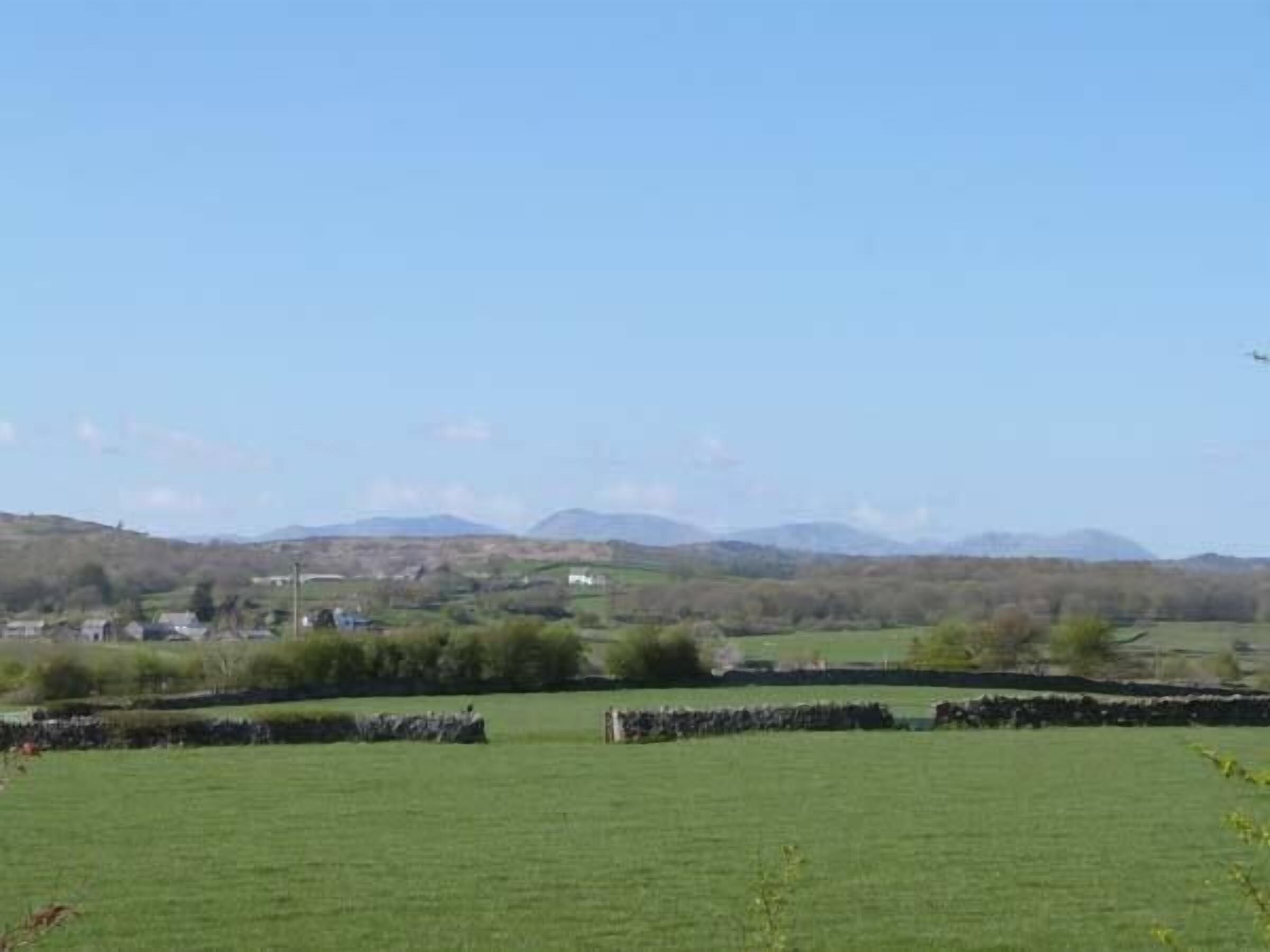 A rural landscape with green fields, stone walls, and distant hills.