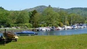 A marina with boats docked along a river, surrounded by lush greenery and hills in the background. - The Byre (Grange-over-Sands)