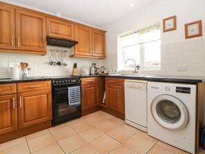 A kitchen with wooden cabinets, a stove, a dishwasher, and a window with curtains.