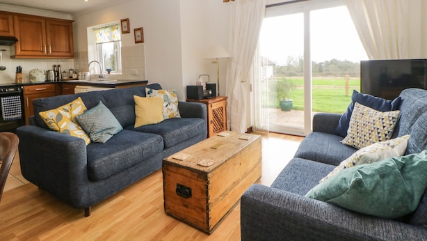 A living room with two sofas, a wooden coffee table, and a kitchen in the background. - Broom Cottage (Sidmouth)