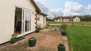 A house with a patio, a sliding glass door, and a small garden with potted plants. - Broom Cottage (Sidmouth)