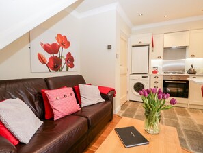 A modern living room with a brown leather sofa, a red and white pillow, a black book, and a vase with purple flowers. - Church View (Ambleside)