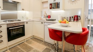 Une cuisine moderne équipée d’une cuisinière à gaz, d’un four et d’un évier. On y trouve un panier de fruits sur le comptoir et une chaise rouge.