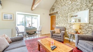 Un salon avec un mur en pierre, deux canapés gris, une table basse en bois et un coin repas comprenant des chaises et une table.