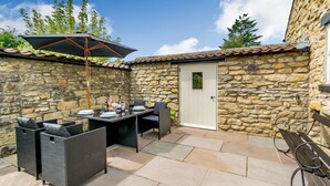 Une terrasse aux murs de pierre, avec une table, des chaises, une porte et un banc.