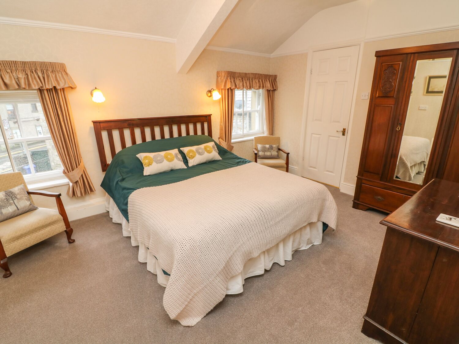 A bedroom with a large bed, a wooden wardrobe, a chair, and a window with curtains.
