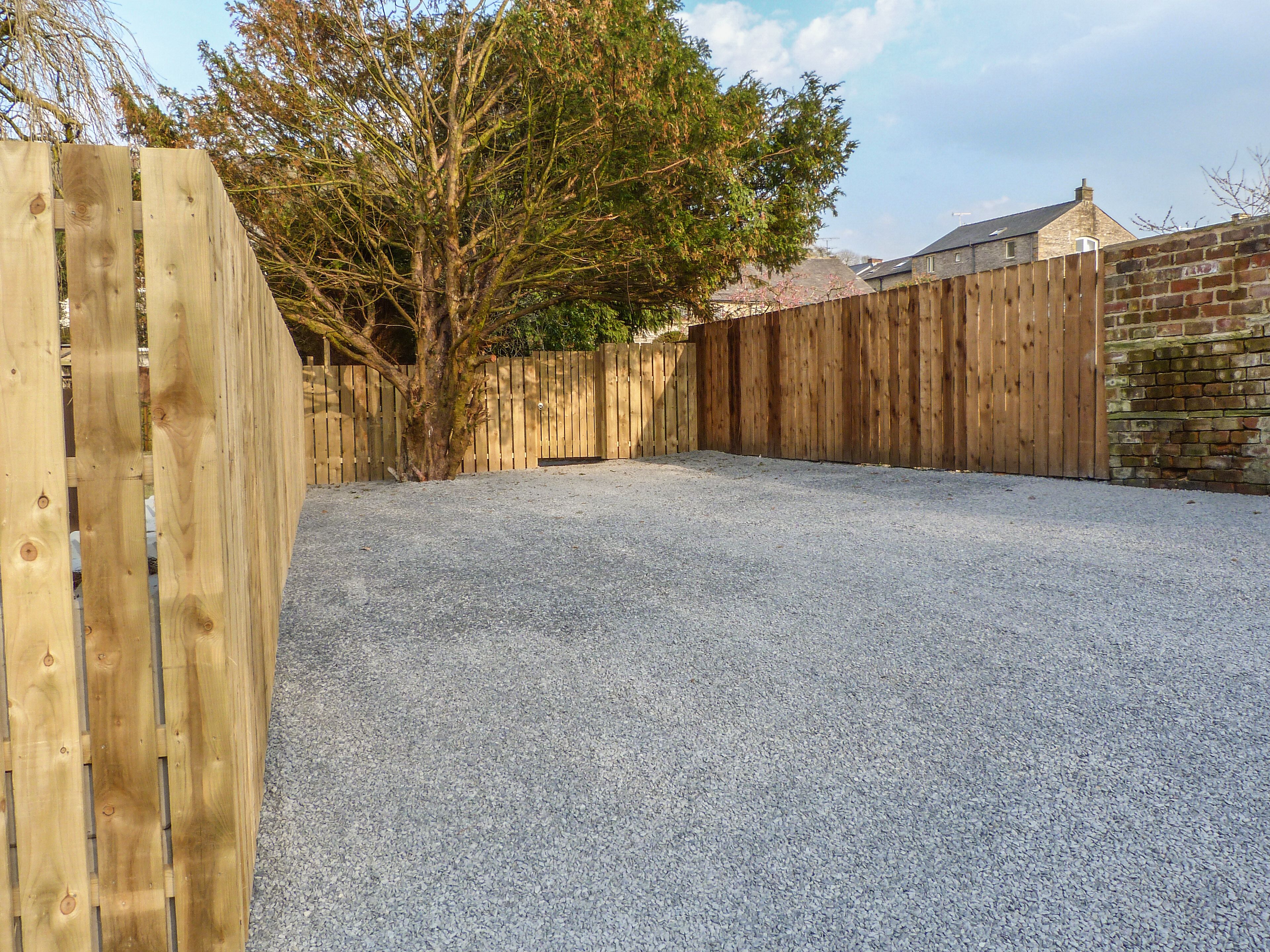 A gravel backyard enclosed by a wooden fence with a tree in the center.