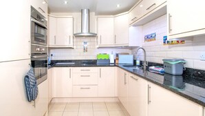A modern kitchen with white cabinets, a stainless steel range hood, a double oven, and a granite countertop. - The Moorings (Conwy)