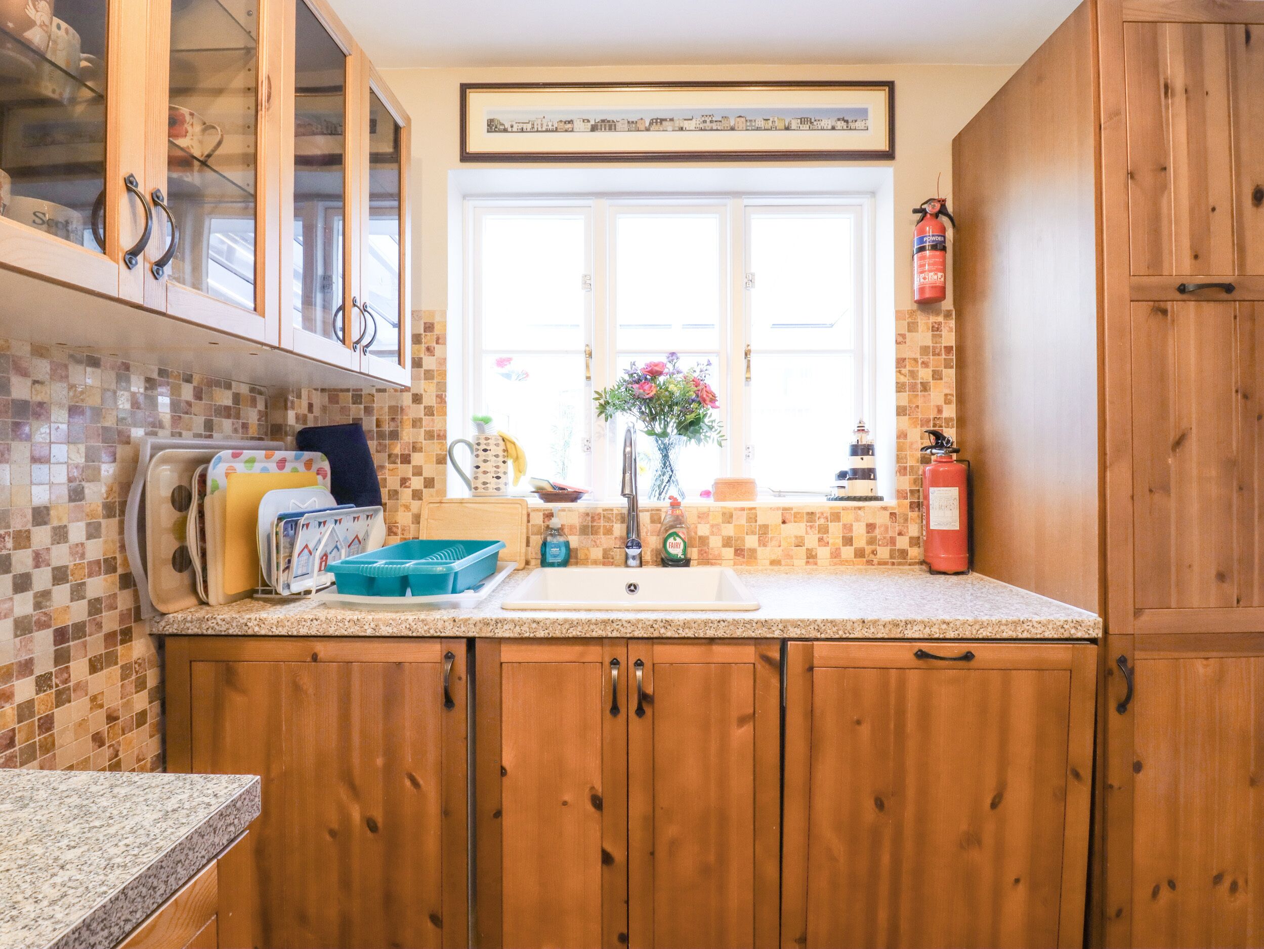 A kitchen with wooden cabinets, a tiled backsplash, a window with a view, and a fire extinguisher.