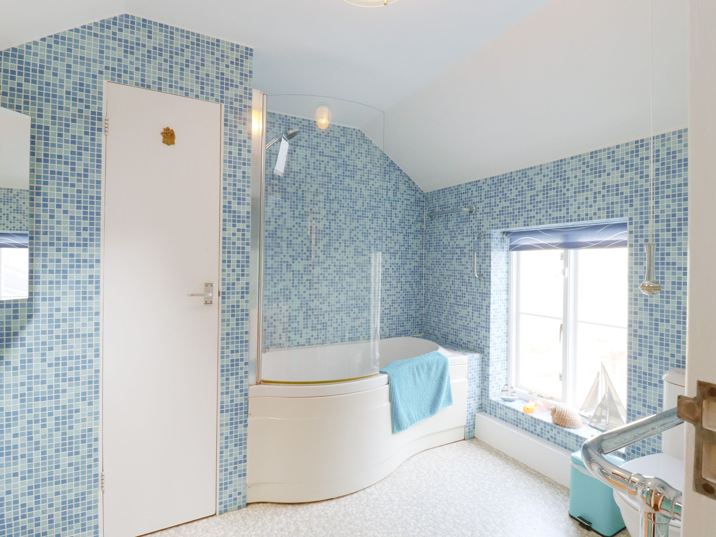 A bathroom with blue mosaic tiles, a white bathtub, a shower, and a window with a view.