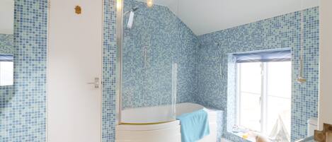 A bathroom with blue mosaic tiles, a white bathtub, a shower, and a window with a view.