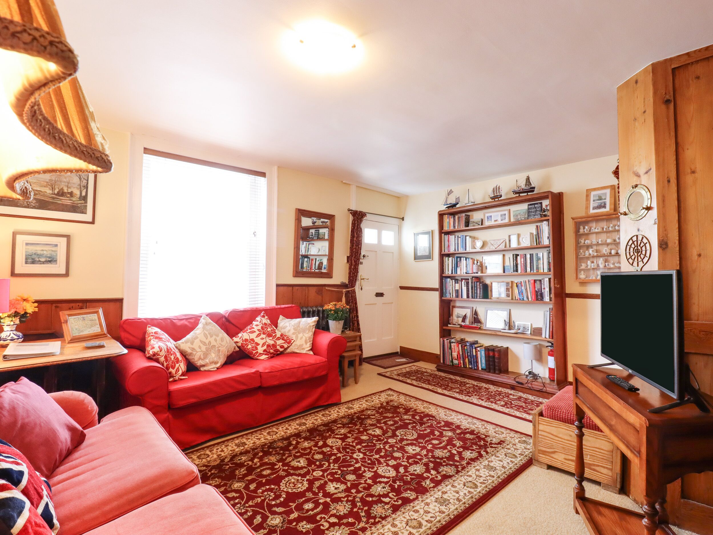 A living room with a red sofa, a bookshelf, a television, and a wooden cabinet.
