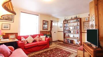 A living room with a red sofa, a bookshelf, a television, and a wooden cabinet.