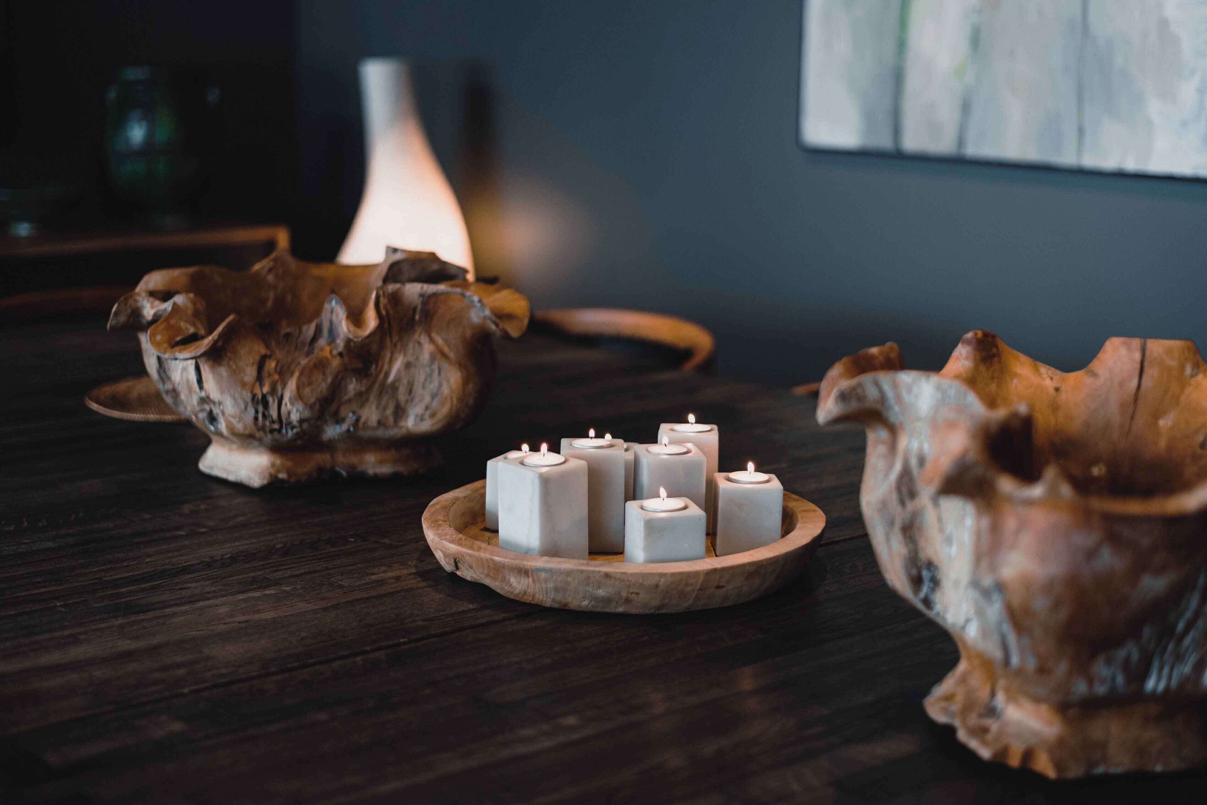 A wooden table with a decorative bowl containing six white candles.