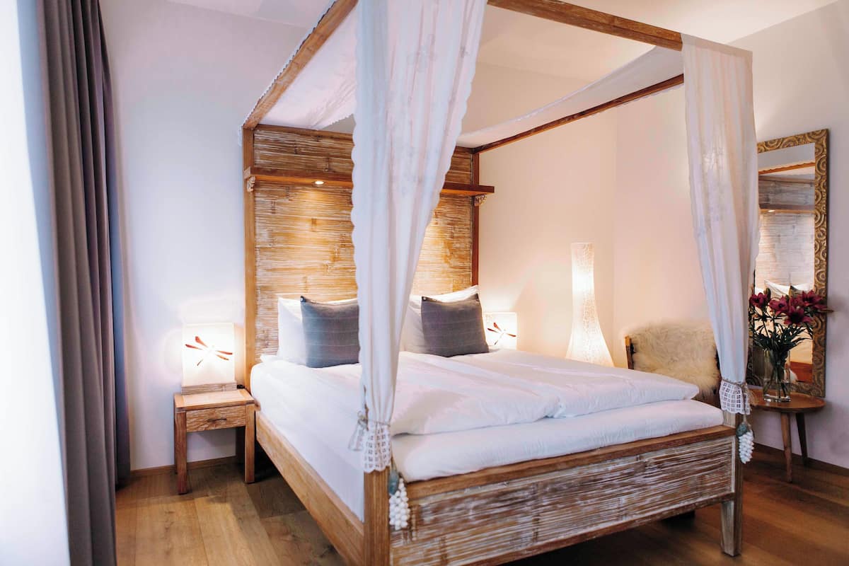 Una cama con dosel con ropa de cama blanca, cabecera de madera y lámparas de noche.