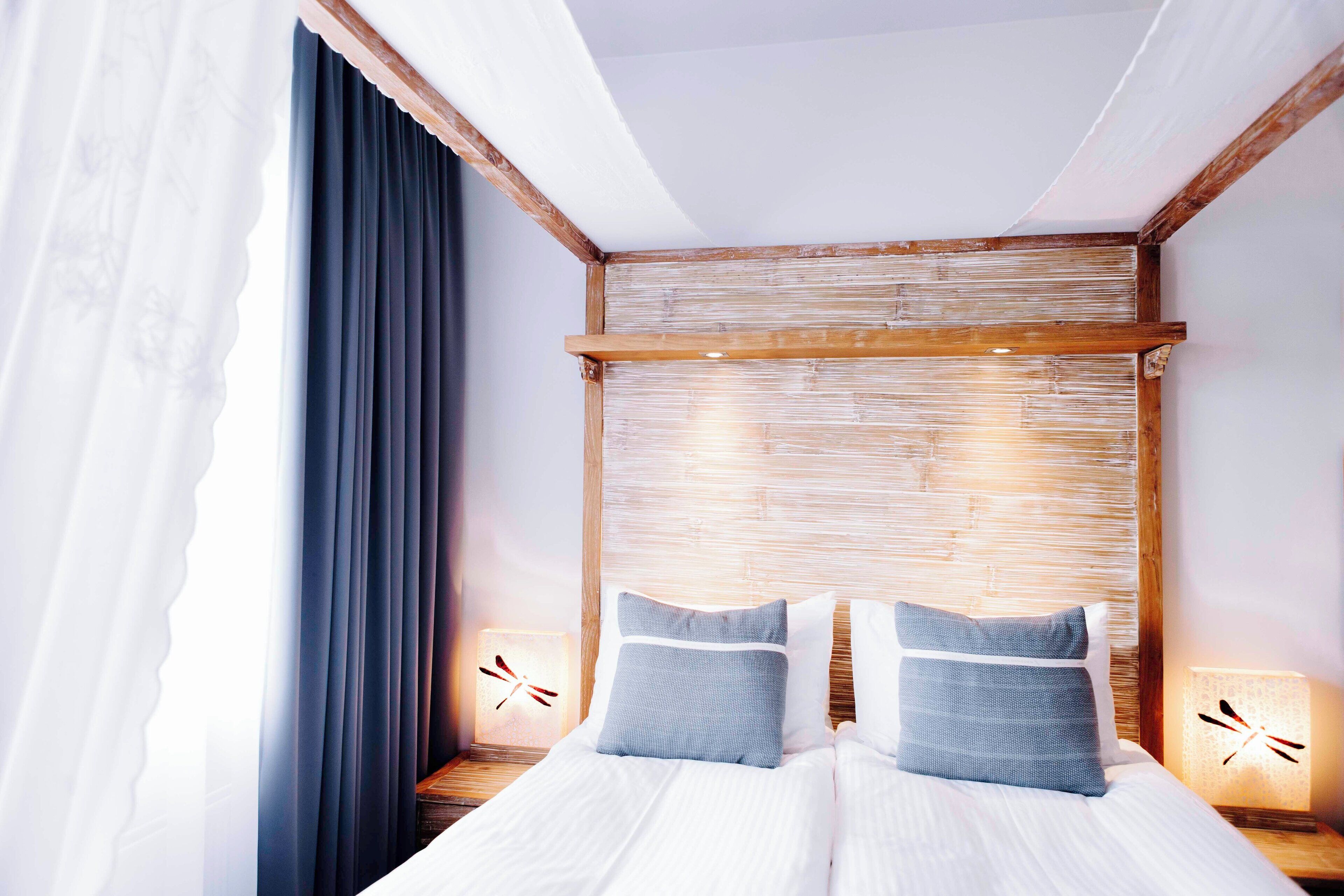 Una cama bien tendida con dos almohadas, un cabecero de madera y lámparas de noche con diseño de libélula.