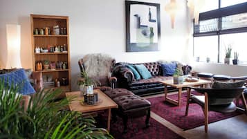 A cozy living room with a leather sofa, a wooden coffee table, and a bookshelf filled with various items.