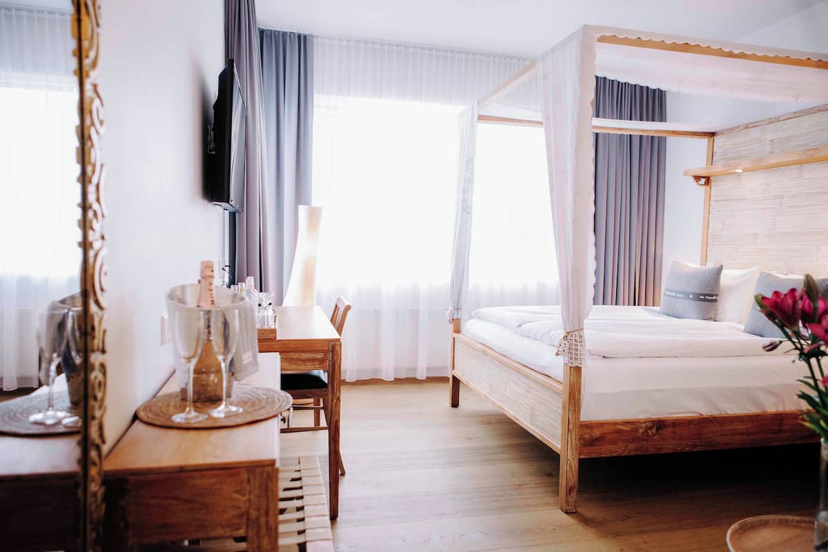 Un dormitorio con cama con dosel, un escritorio de madera con silla, un espejo y una mesita de noche con un jarrón de flores.
