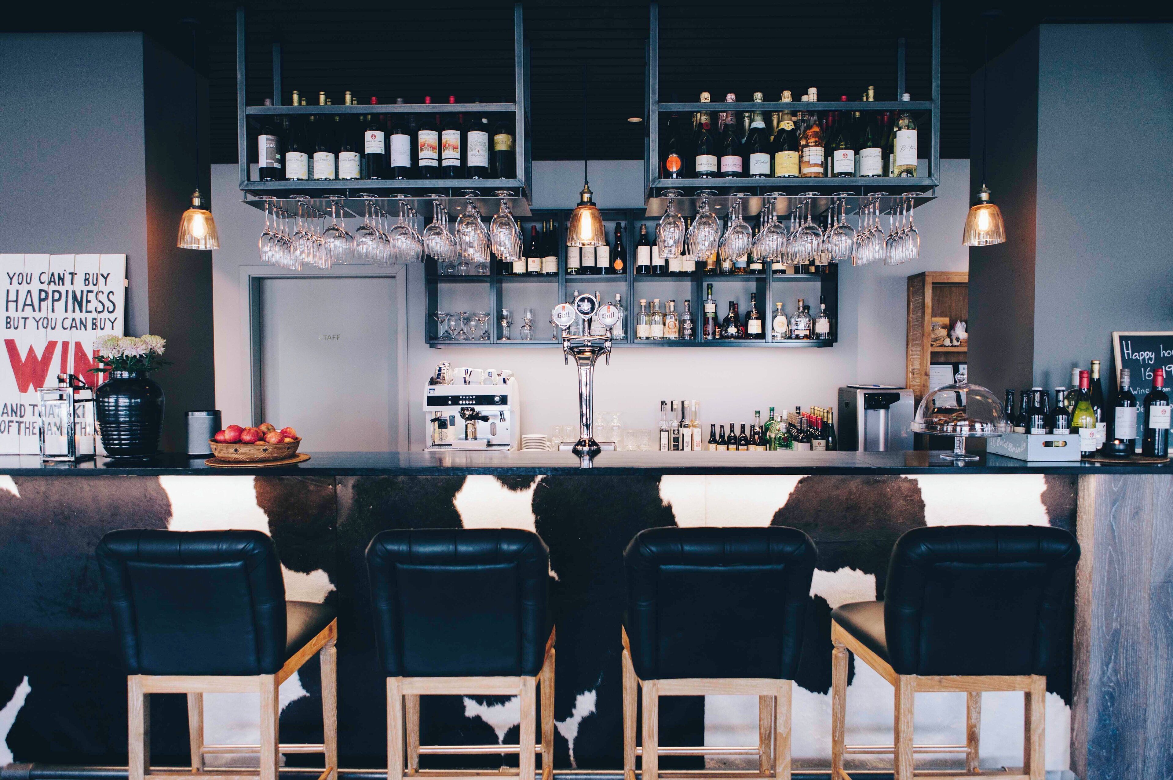 A bar area with a counter, shelves of bottles, glasses, and a sign that reads "YOU CAN'T BUY HAPPINESS BUT YOU CAN BUY WIN."