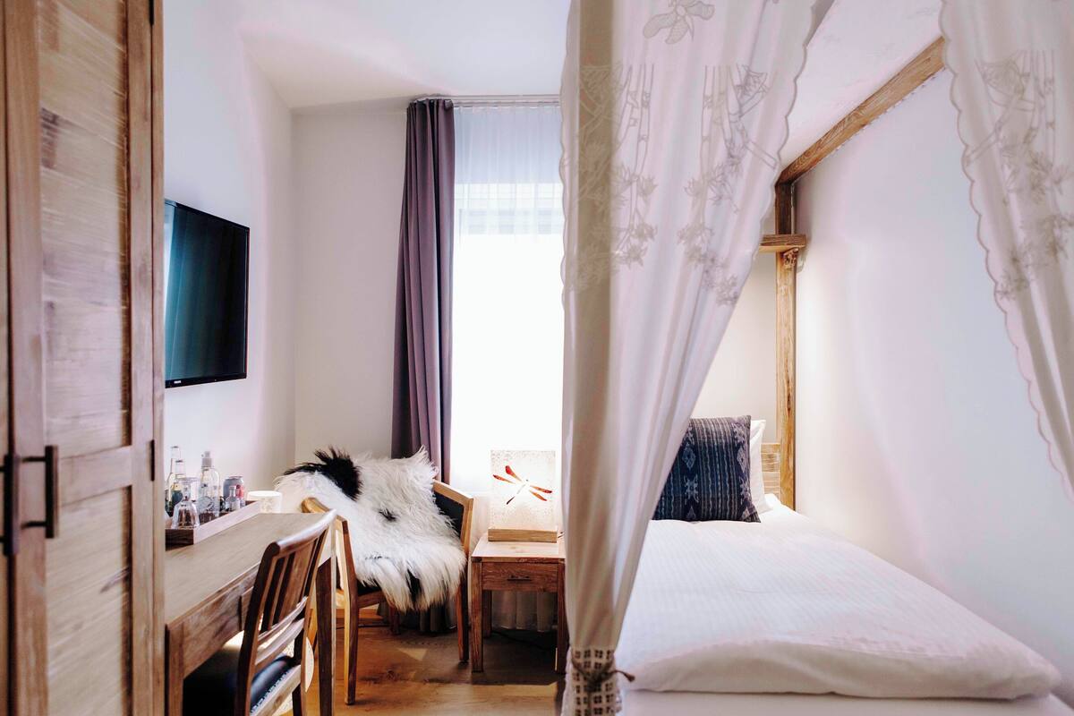 Un dormitorio con cama, escritorio, silla, televisor y ventana con cortinas.