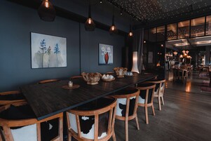 Un lungo tavolo da pranzo con sedie di legno, circondato da opere d'arte, e un'area bar sullo sfondo.