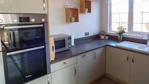 Una cocina con horno empotrado, microondas y armarios de madera.