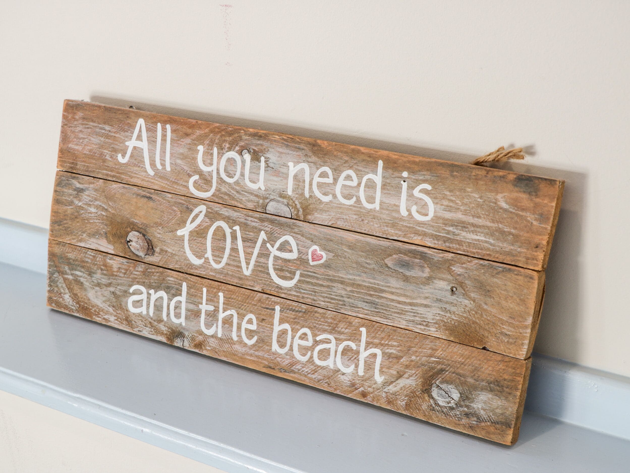 Un letrero de madera con el texto 'Todo lo que necesitas es amor y la playa' colgado en una pared.