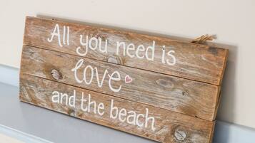 Un letrero de madera con el texto 'Todo lo que necesitas es amor y la playa' colgado en una pared.