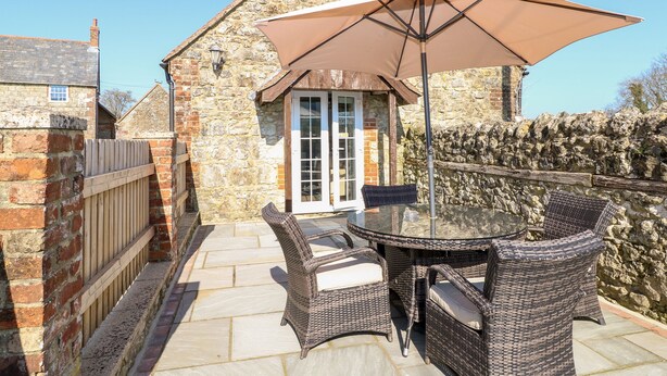 A stone building with a tiled patio, wicker furniture, and a large umbrella. - Stable Cottage (Newport)