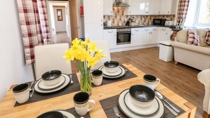 A modern kitchen with white cabinets, a stainless steel range hood, and a dining area with a wooden table set for four. - Stable Cottage (Newport)