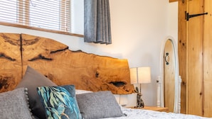 A bedroom with a large wooden headboard, a bed with floral bedding, and a nightstand with a lamp and a rabbit figurine. - The Lodge (Chester)