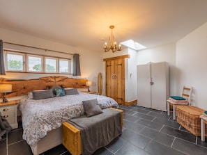 A bedroom with a large bed, a wooden headboard, a wardrobe, a chest of drawers, a small table, a chair, and a window with blinds. - The Lodge (Chester)