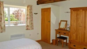 A bedroom with two beds, a wooden dresser, a mirror, and a window with curtains. - Byre Cottage (Shrewsbury)