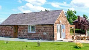 A stone building with a sloped roof, a small porch with chairs, and a grassy yard. - Byre Cottage (Shrewsbury)