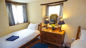 Un dormitorio con una cama individual, un aparador de madera con dos lámparas y una ventana con cortinas.