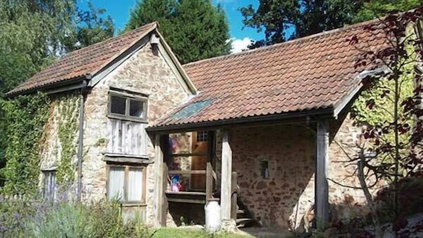 Una casa de piedra con techo de tejas, puerta de madera y un ventanal pequeño.
