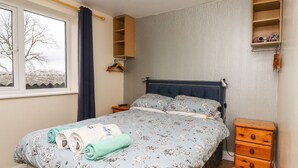 Une chambre à coucher comprenant un lit, une table de chevet, une armoire, une fenêtre avec des rideaux et une vue sur les arbres à l’extérieur.