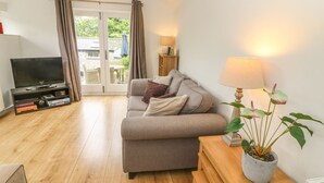 A cozy living room with a sofa, a TV, a lamp, and a potted plant. - The Potting Shed (Carnforth)