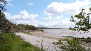 A coastal landscape with a sandy beach, grassy areas, and a rocky cliff. - The Potting Shed (Carnforth)