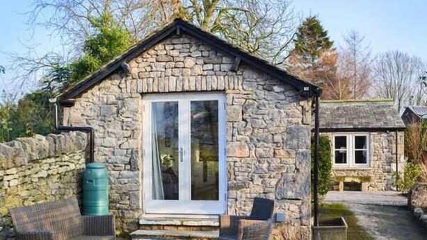 A stone cottage with a small patio, two wicker chairs, and a large water tank. - The Potting Shed (Carnforth)