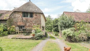 A rustic stone house with a thatched roof, a gravel path leading to a wooden gate, and chickens in the foreground. - The Dairy (Taunton)