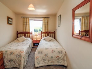 Two single beds with wooden headboards and matching bedding, a large mirror, and a window with a view.