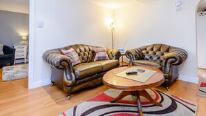 A living room with a brown leather sofa, a wooden coffee table, and a red and white striped rug. - Mermaid Cottage (Whitby)