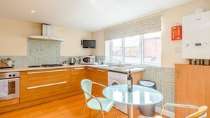 A modern kitchen with wooden cabinets, a glass dining table, and a built-in microwave. - Mermaid Cottage (Whitby)