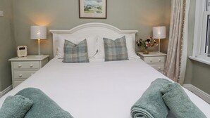 Cama bem arrumada com duas almofadas, duas luminárias de cabeceira, um quadro na parede e uma janela com cortinas.