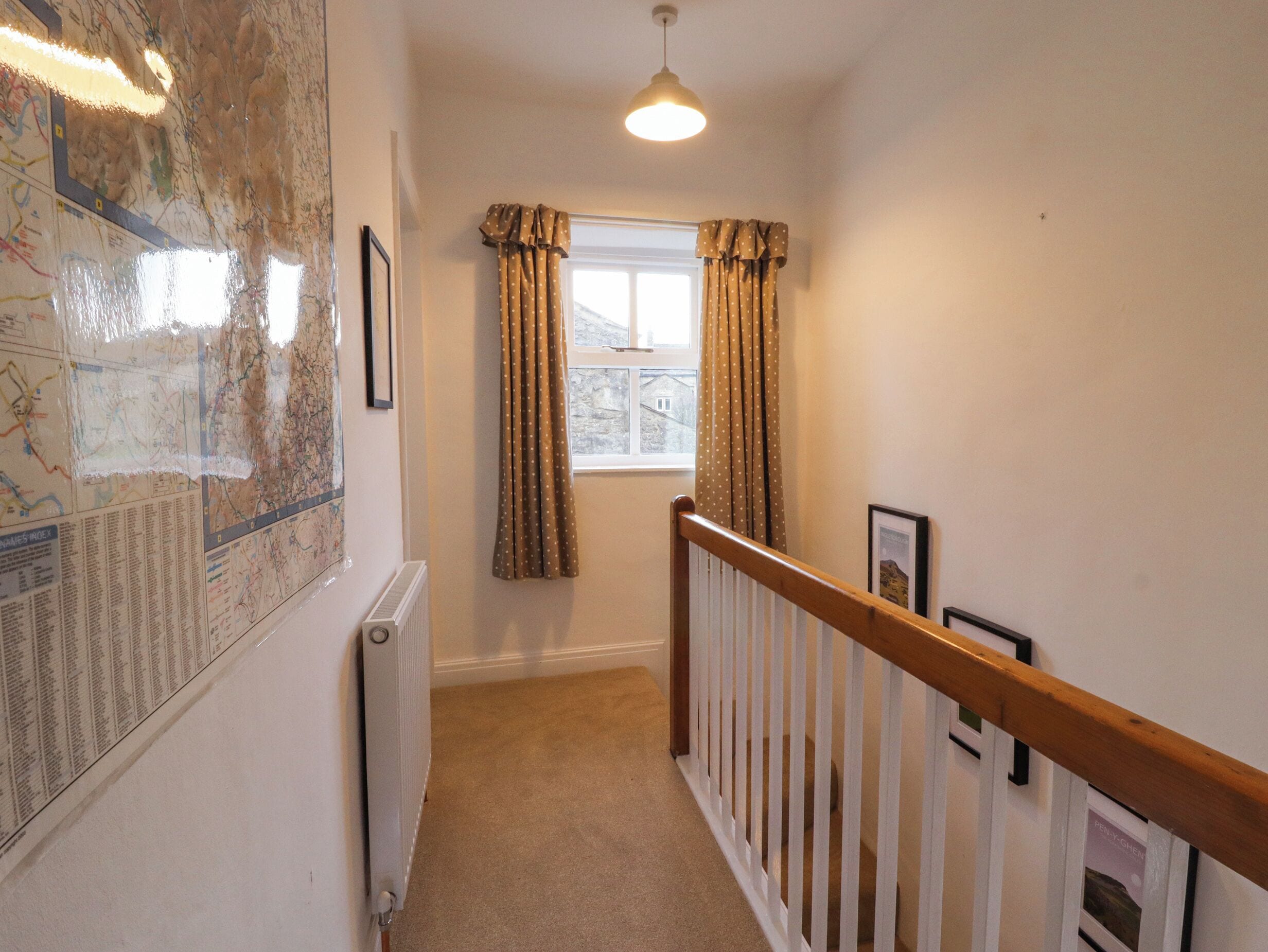 A narrow hallway with a radiator, a window with curtains, a wooden railing, and a map on the wall.