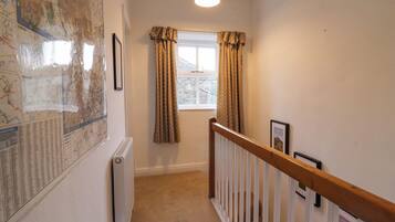 A narrow hallway with a radiator, a window with curtains, a wooden railing, and a map on the wall.