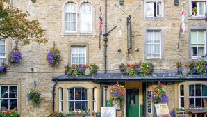 A stone building with flower boxes, outdoor seating, and flags. - Lavender Cottage (Skipton)